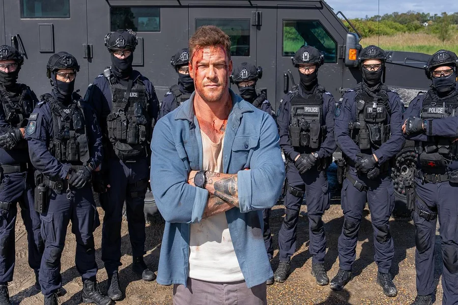 Alan Ritchson standing in a doorway, broad-shouldered and towering, conveying the imposing presence of Jack Reacher