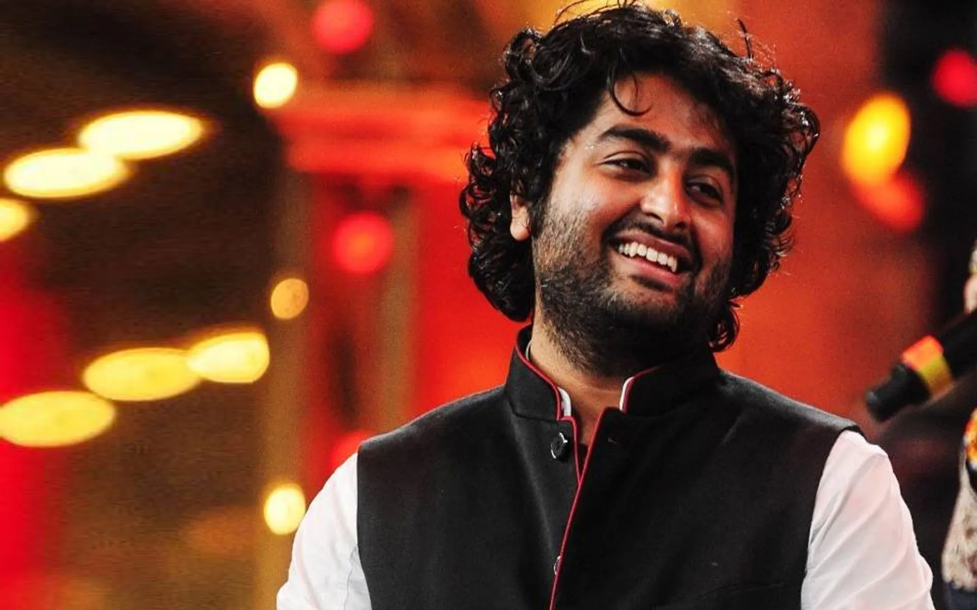 Arijit Singh performing under soft stage lights, microphone in hand, with a calm expression
