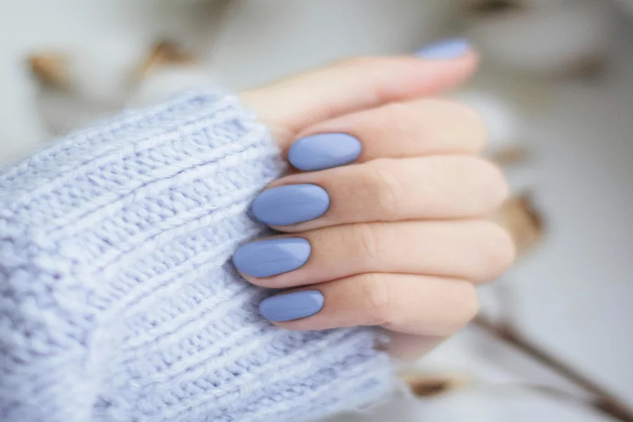 Hand in a knit sweater holding a warm beverage with glossy navy blue winter manicure