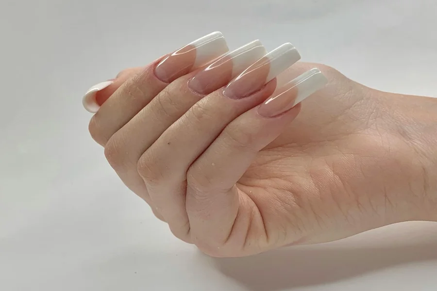 Close up of hands with modern French tip nails featuring a sheer base and slim, glossy white edges on oval shaped nails