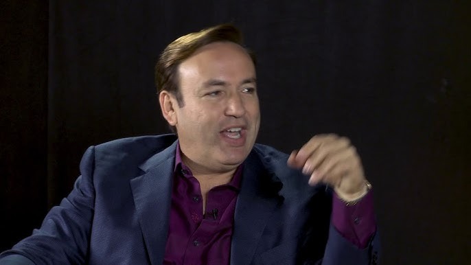 A composed portrait of Javier Romero in a public setting, showing confident posture, direct gaze, and polished styling under soft lighting.