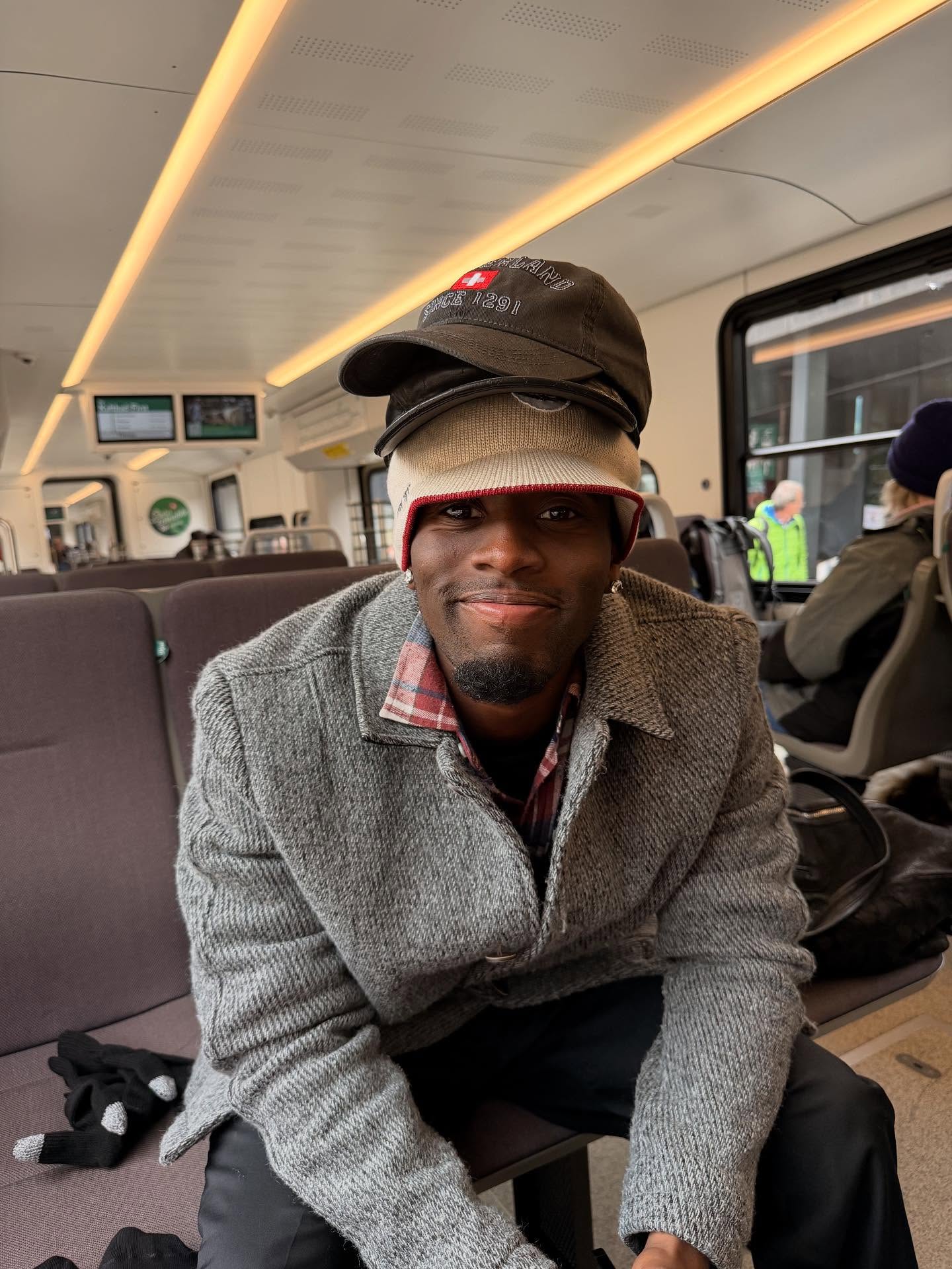 Kai Cenat smiling on a streaming set, standing next to a taller guest with studio lights in the background