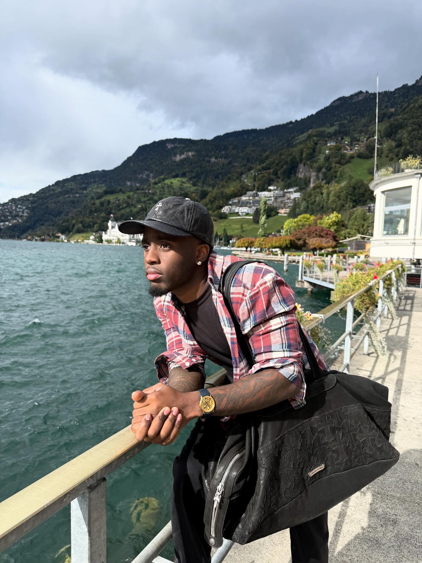 Kai Cenat smiling on a streaming set, standing next to a taller guest with studio lights in the background