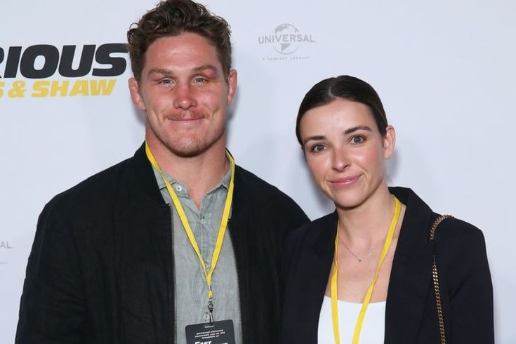 Kate Howard stands beside Michael Hooper at a public event, poised and elegant with a confident smile.