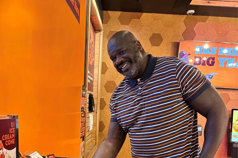 Shaquille O’Neal towering over a crowd of average-height people, highlighting his 7-foot-plus stature