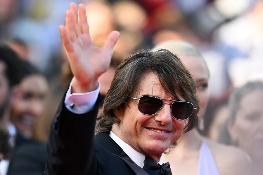 Tom Cruise standing on a red carpet, appearing taller through camera angle and footwear