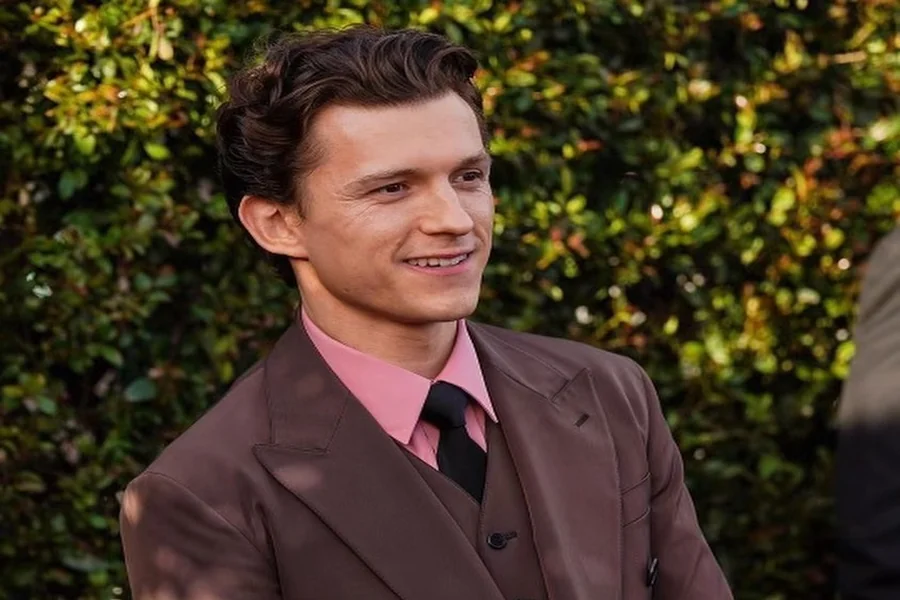 Tom Holland on a red carpet in a tailored suit, standing confidently beside Zendaya who is wearing heels