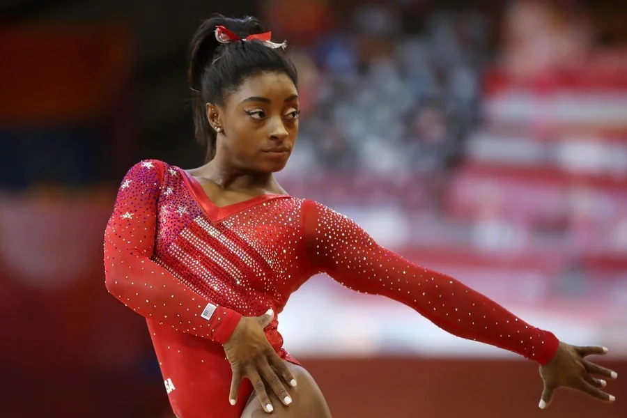 Simone Biles mid air during a floor routine, showing power, precision, and control