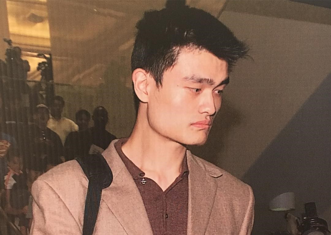 Yao Ming, a 7-foot-6 center, standing courtside with a calm expression, highlighting his towering height and composed presence