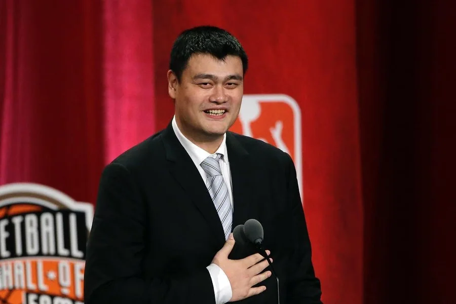 Yao Ming, a 7-foot-6 center, standing courtside with a calm expression, highlighting his towering height and composed presence